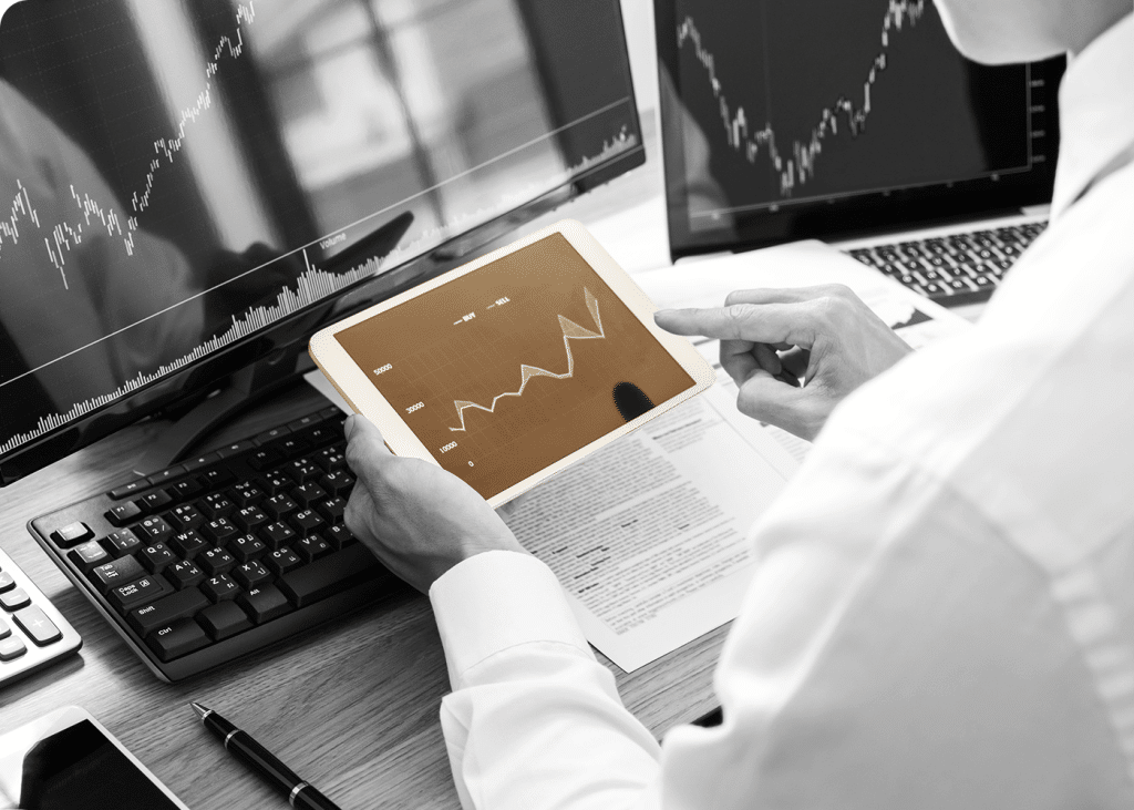 Professionnel analysant des graphiques boursiers sur une tablette et des écrans d'ordinateur.