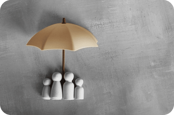 Figurines sous un parapluie beige, représentant la protection des assurances collectives.