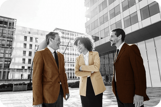 Trois professionnels en costume discutant à l'extérieur d'un bâtiment moderne.